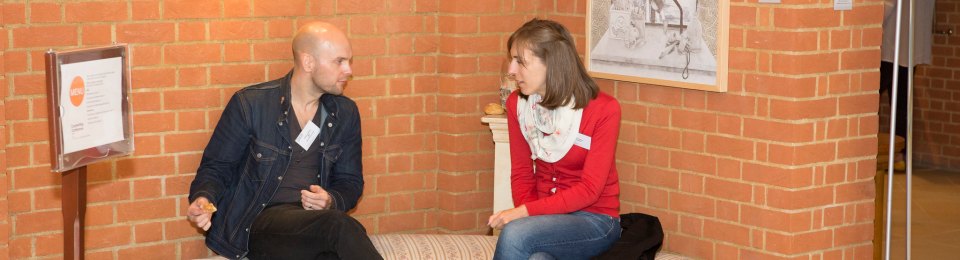 Two people at a conference chatting while sitting on a bench in a corner.